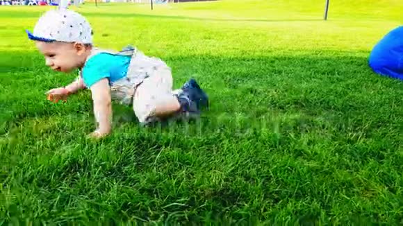 在一个温暖的夏日两个婴儿在明亮的绿草上爬行视频的预览图