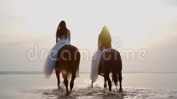 日落时两个穿着白色连衣裙的女孩骑马在水上散步视频的预览图