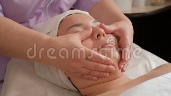 抗衰老面部按摩一位专业美容师的双手光滑了一个亚洲女孩脸上的皮肤SPA视频的预览图