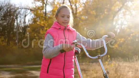秋天一个骑自行车的孩子在温暖的阳光下在公园里散步一个年轻的女孩在路上滚动自行车视频的预览图