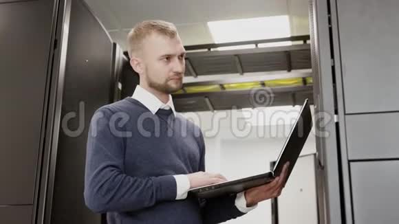 系统管理员手持笔记本电脑站在服务器机架前视频的预览图