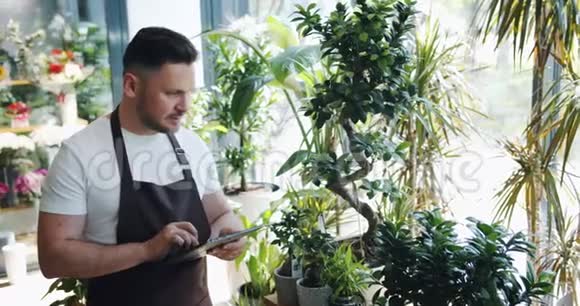 快乐的男花商在花店里用平板电脑工作微笑着看着植物视频的预览图