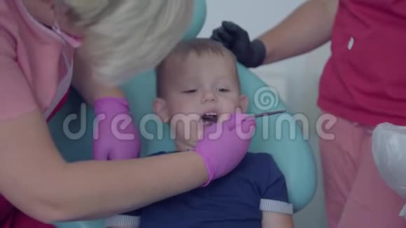 戴着医用口罩和手套的牙医检查坐在椅子上的无忧无虑的小男孩的牙齿淘气的病人视频的预览图