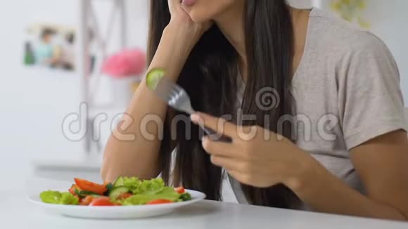 伤心的女孩在家吃沙拉没有食欲冷漠蔬菜饮食无聊视频的预览图