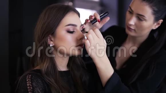 化妆师做专业的化妆年轻的女人留着长发穿着黑色的衣服玛斯卡拉用长睫毛视频的预览图