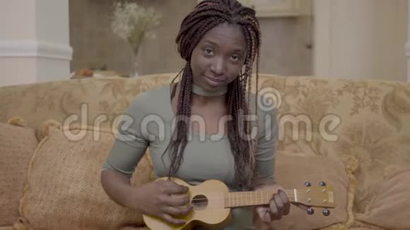 在现代客厅里漂亮的非洲裔美国妇女在教练身上弹着四弦琴吉他视频的预览图