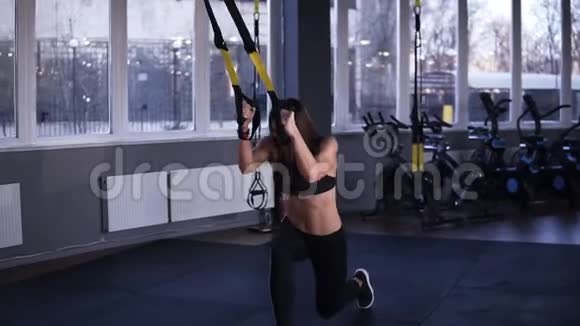 肌肉发达穿着黑色运动服的健身女孩在拿着肩带做腿部运动挤压粘合腿视频的预览图