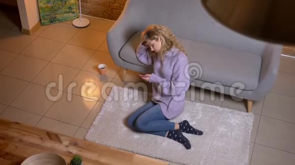 成人白种人金发女性在坐在地板上靠在沙发上时使用手机的特写镜头视频的预览图