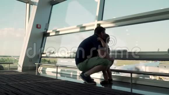 父子俩透过玻璃窗看着飞机在机场和婴儿一起旅行视频的预览图