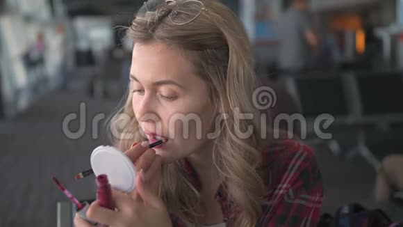 一个年轻漂亮的女孩穿着一件红色的格子衬衫坐在侧面用红色的口红画出她的嘴唇视频的预览图