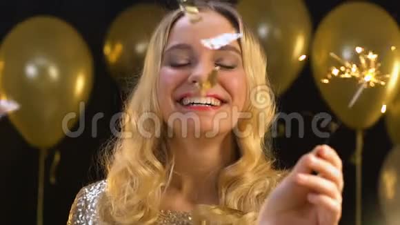微笑的金发女人在飘落的纸屑下挥舞着孟加拉灯新年晚会视频的预览图