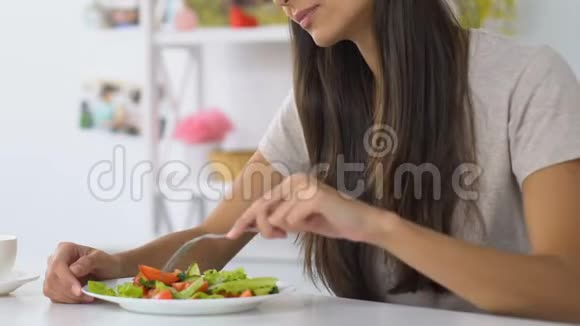 坐在舒适的厨房里享受新鲜蔬菜沙拉的年轻女子视频的预览图