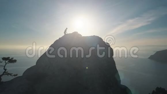 夕阳西下一位年轻女子爬上山顶靠海的空中轮廓出席峰会的女士视频的预览图