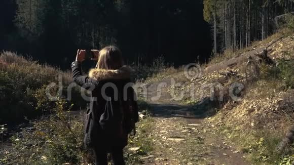 年轻女孩徒步旅行者正在用手机摄像机拍摄美丽的森林景观和河流视频的预览图
