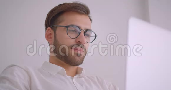 戴着眼镜长着胡子的白种人英俊商人的特写镜头用笔记本电脑看着镜头开心地笑着视频的预览图
