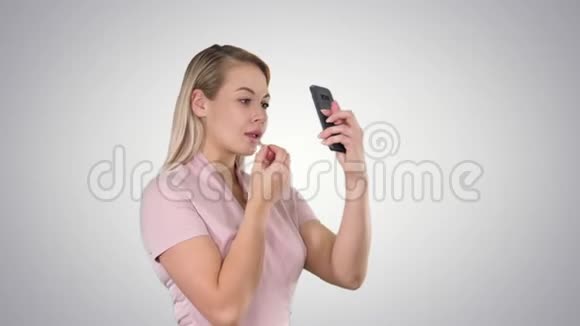 美女人化妆年轻的女人嘴唇看着梯度背景上的智能手机视频的预览图