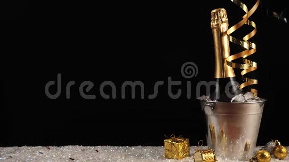 好香槟酒瓶子与起泡葡萄酒在一个桶与真正的冷冰在白雪黑背景金色彩带视频的预览图