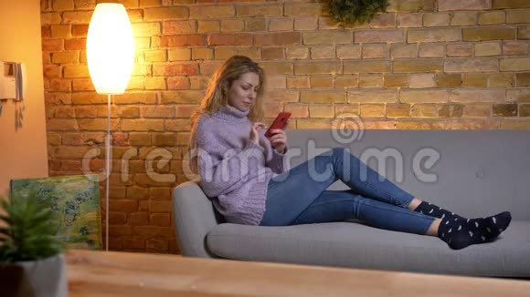 成年白种人金发女性躺在沙发上悠闲地伸腿时使用手机的特写镜头视频的预览图