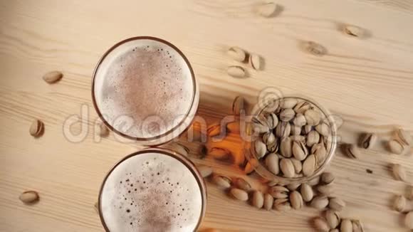 新鲜啤酒背景上的木桌上放着两个玻璃杯杯中放着美味的冷啤酒和一些开心果视频的预览图