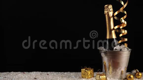 好香槟酒瓶子与起泡葡萄酒在一个桶与真正的冷冰在白雪黑背景金色彩带视频的预览图
