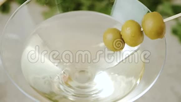 豪华马提尼手把三个绿色橄榄放在鸡尾酒棒上把马提尼放在桌子上视频的预览图