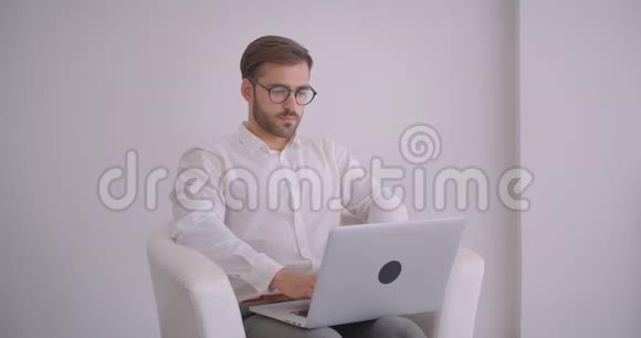 戴着眼镜长着大胡子的白种人成年商人的特写镜头用笔记本电脑看着镜头微笑视频的预览图