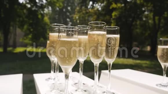 带有气泡的香槟酒杯站在自然背景的白色桌子上慢动作视频的预览图