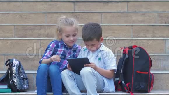 在露天课间休息时学童们用数字平板电脑与背包坐在台阶上视频的预览图