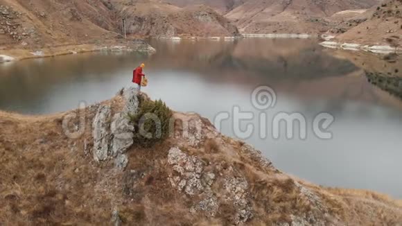 鸟瞰一个女孩坐在湖岸的岩石上旅行录像视频的预览图