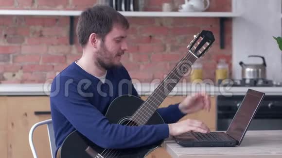 开朗的音乐家练习弹吉他使用笔记本电脑和在线视频教程和快乐音乐视频的预览图