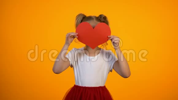 漂亮的女孩躲在红纸心后面对着镜头微笑情人节爱视频的预览图