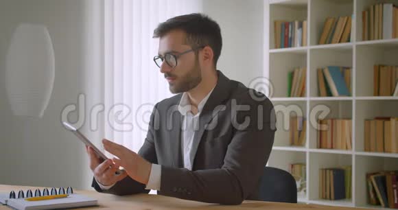用平板电脑拍摄成年英俊白种人商人眼镜的特写肖像并用绿色屏幕拍摄视频的预览图
