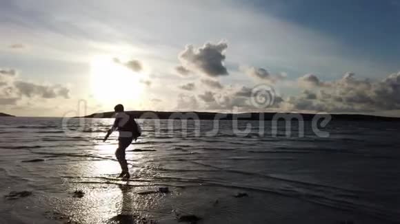 日落时沿着海滩漫步的女士剪影视频的预览图