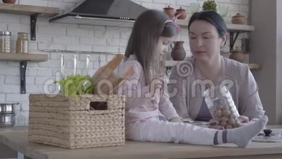 坐在桌子旁的小有趣的女孩帮她祖母做蛋糕站在桌子旁边的一位老妇人视频的预览图