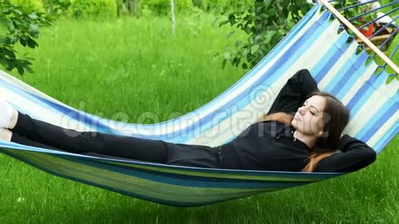 美丽的年轻女子躺在花园里的吊床上休息和打瞌睡视频的预览图