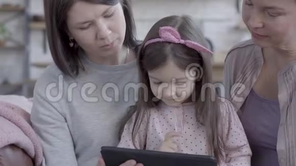 三代女人坐在沙发上聊天看着小女孩如何在平板电脑里玩游戏视频的预览图