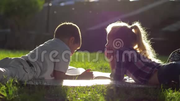 初恋美丽的小男孩和女孩躺在草地上在学校休息时在户外看一本书视频的预览图