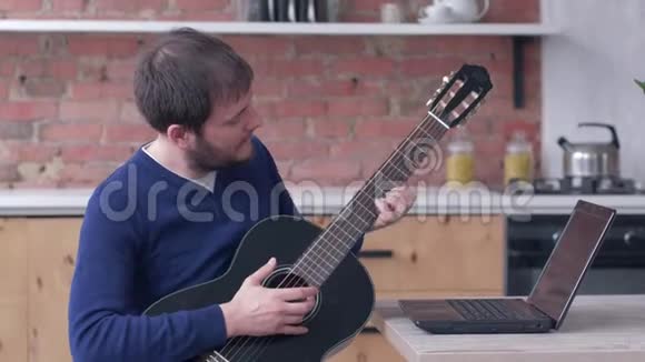 有趣的器乐演奏家男性学习吉他使用笔记本电脑在线视频培训和享受音乐视频的预览图