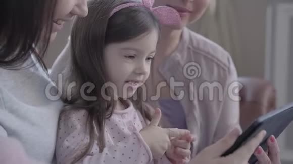 三代女人坐在沙发上聊天看着小女孩如何在平板电脑上玩游戏视频的预览图