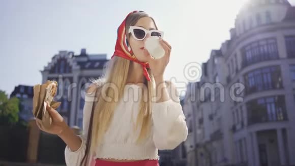 肖像美丽的年轻女子走在街上喝咖啡吃牛角面包漂亮的时髦女孩视频的预览图