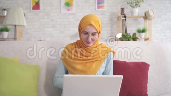 积极的年轻穆斯林妇女手提电脑坐在客厅的沙发上看着相机微笑视频的预览图