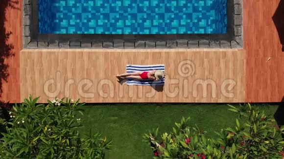 在热带地区穿着红色比基尼戴着草帽用毛巾在游泳池附近晒日光浴视频的预览图