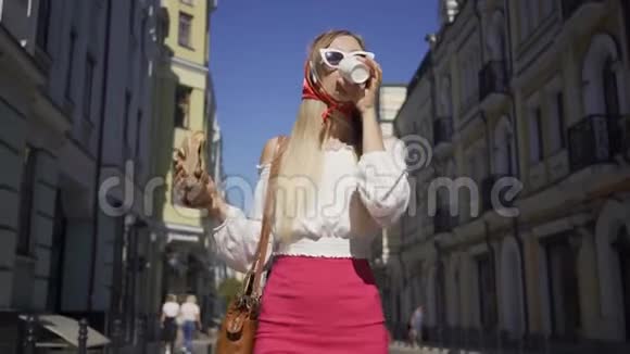 美丽的年轻女子走在街上喝着咖啡吃着牛角面包很有魅力的时尚女孩视频的预览图