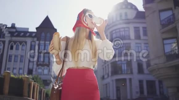 肖像可爱的年轻女子走在街上喝咖啡吃牛角面包漂亮的时髦女孩视频的预览图