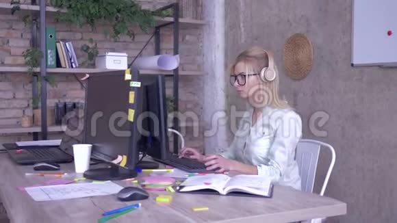 戴眼镜和戴耳机的女工在现代创意办公室工作视频的预览图