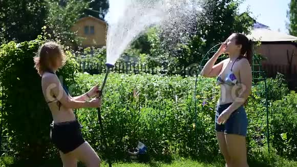 夏天阳光明媚的一天两个年轻漂亮的女孩从花园的软管里互相倒在绿色的草坪上穿短短裤的金发美女视频的预览图