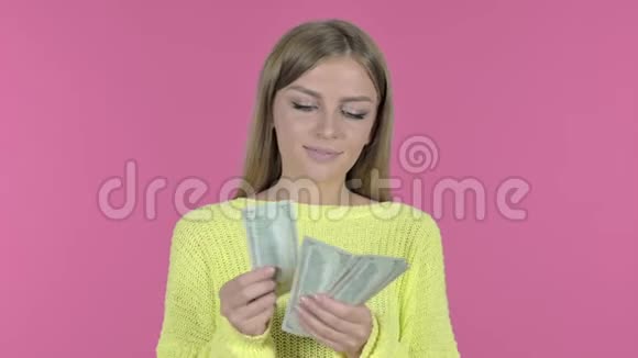 活泼开朗的年轻女孩数钱粉色背景视频的预览图