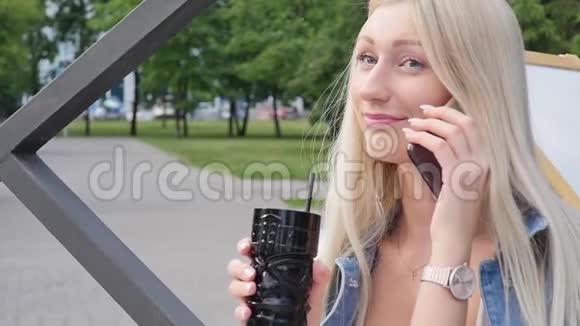 漂亮的金发女郎在咖啡馆里吃午饭时正在打电话她微笑着有智能手机的年轻女子视频的预览图