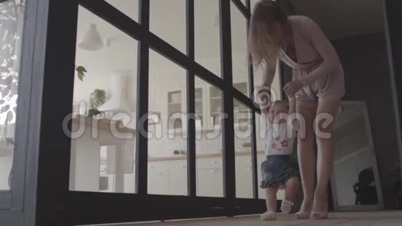 可爱的女人和她的女婴站在家里的地板上孩子迈出第一步妈妈支持她妈妈玩游戏视频的预览图