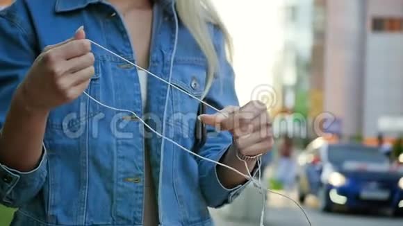 一个年轻的女人试图解开长长的白色耳机线一位金发女郎手中拿着科学老师的画像视频的预览图
